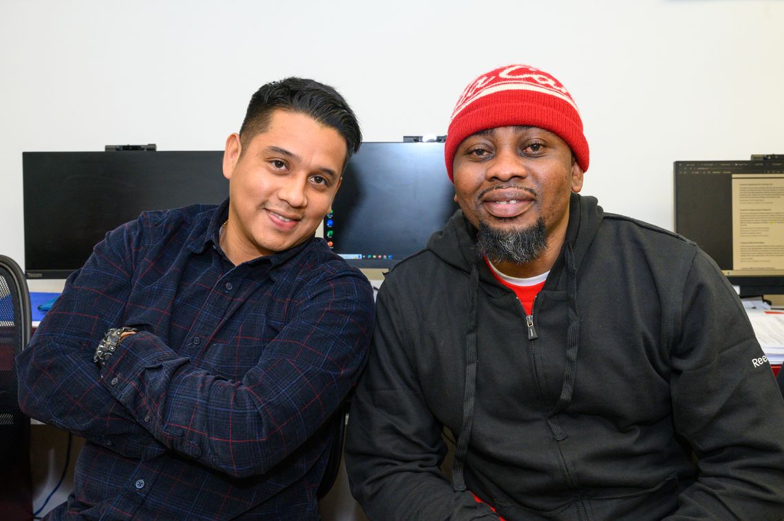 two men smiling in front of computer screens