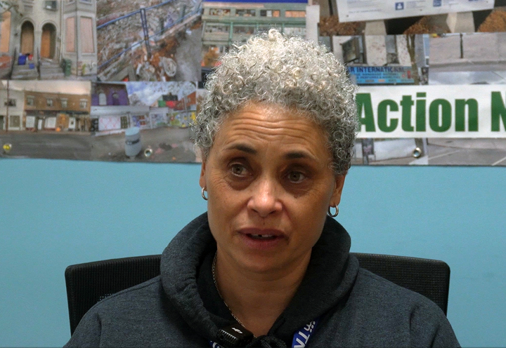 middle age woman sitting and talking with the word "action" and photos on the wall behind her