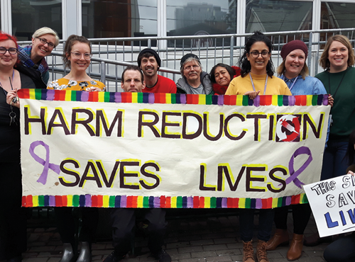 people posing with banner saying harm reduction saves lives
