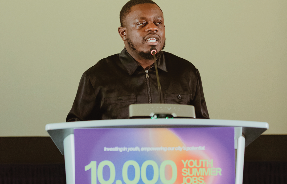 man standing in front of a podium with 10,000 Youth Summer Jobs poster